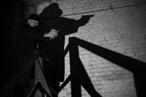 Man holding gun at top of stairs with deep shadows on wall